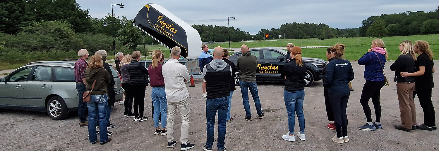 Många människor med ryggen mot kameran tittar på Ingelas för körkort bil med släp.